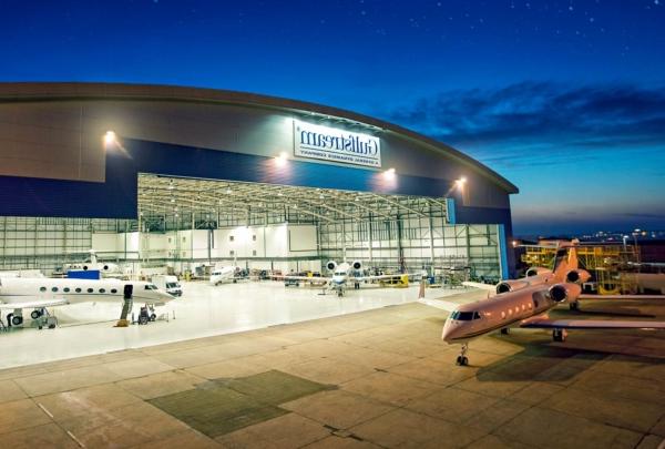 Exterior of Gulf Stream Service Center at night. Planes inside hangar 和 outside on apron.