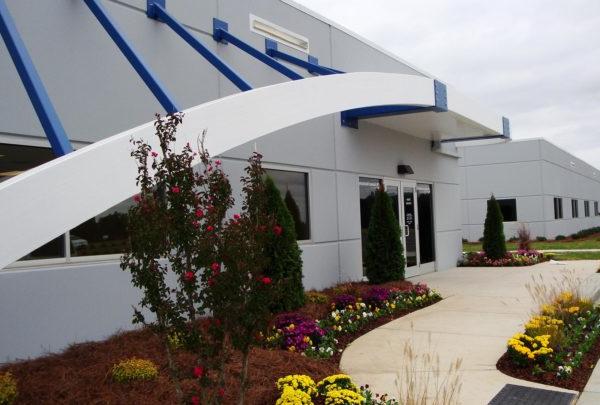 Front entrance of Turbomeca TMM 澳门足彩app Facility. Awning supported by blue structures. Floral l和scaping.